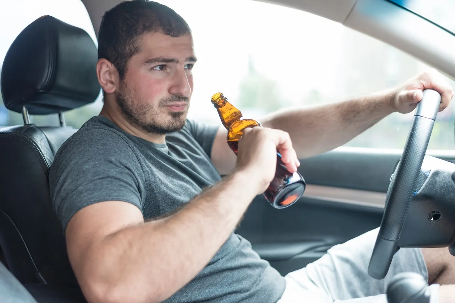 Man driving while holding a beer bottle