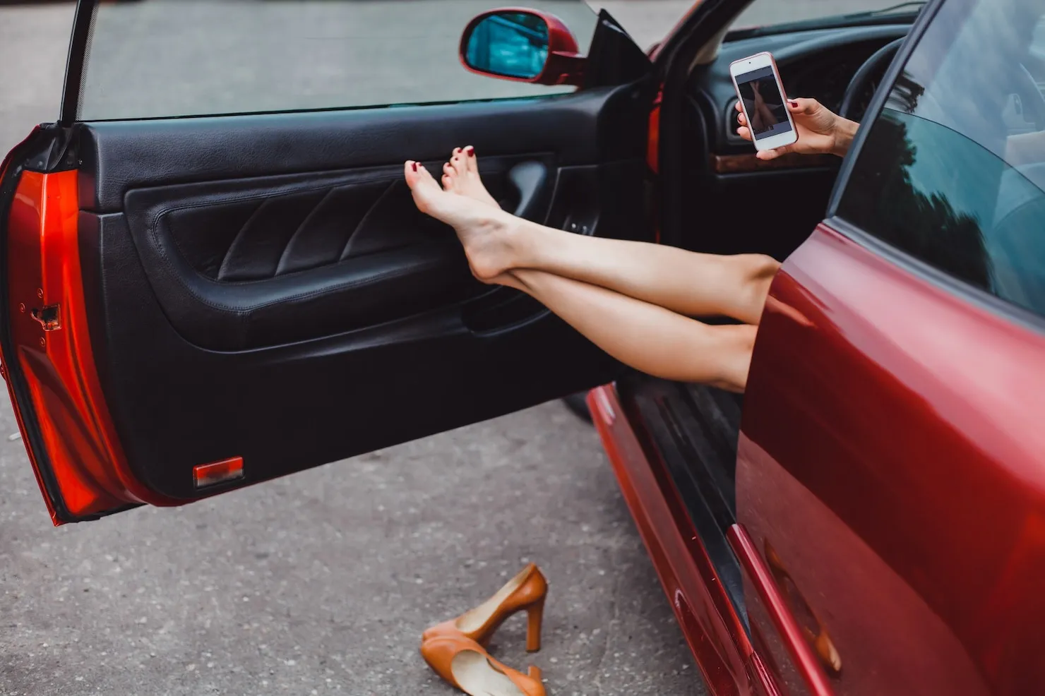 Woman sitting in car with legs out and holding a phone